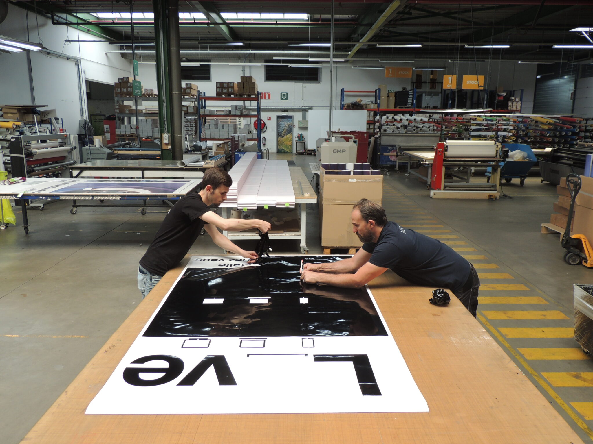 Twee medewerkers werken een grote gedrukte print af op de afwerkingstafel